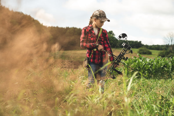 Photo of a young girl in black and red plaid shirt holding a PSE kid's bow.