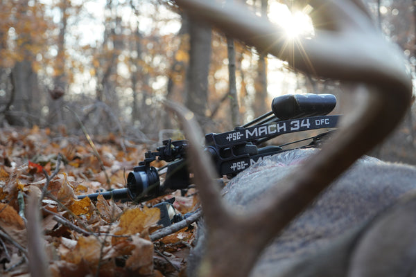 PSE Carbon hunting bow Mach 34 rests against a whitetail deer in the woods.